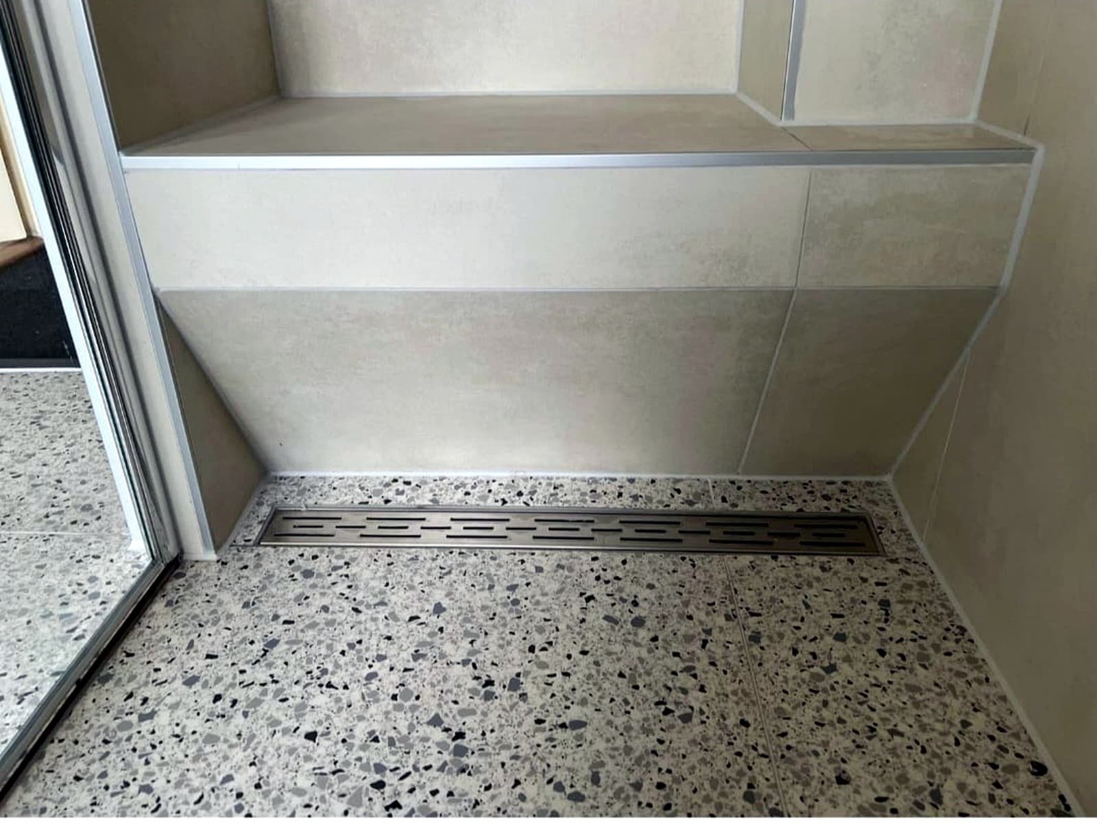 Terrazzovloer met een lange vloergoot langs de betegelde zitbank