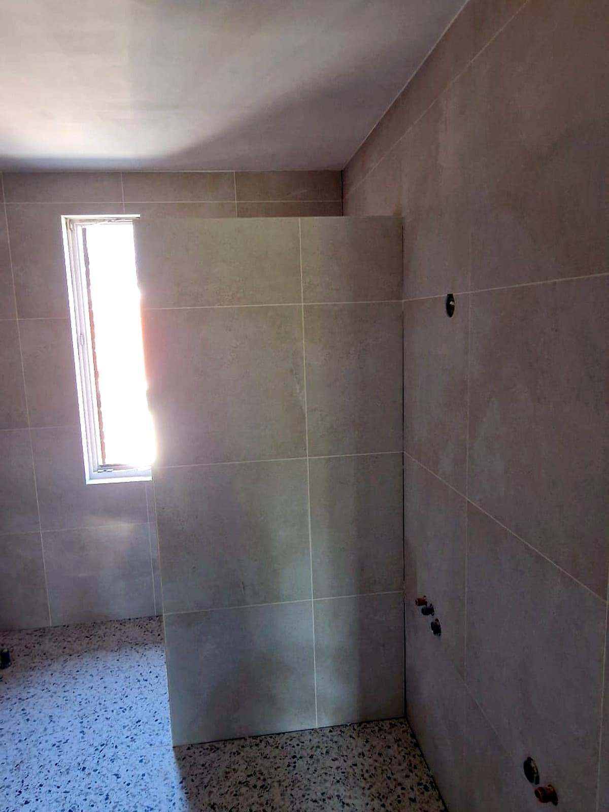 Terrazzovloer met lichte wandtegels in een douche in aanbouw