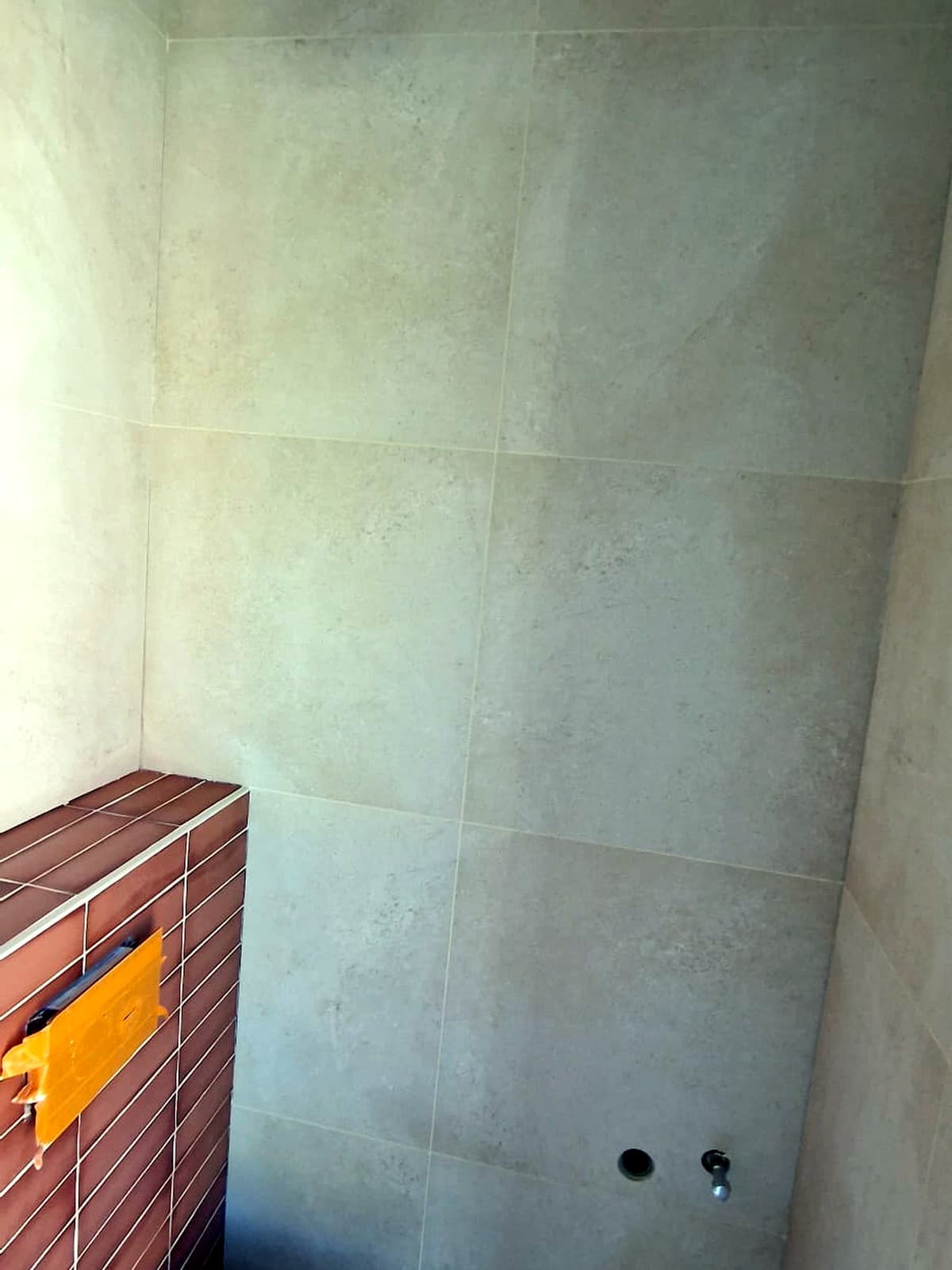 Toiletwand in aanbouw met lichte wandtegels en roodbruine strooktegels