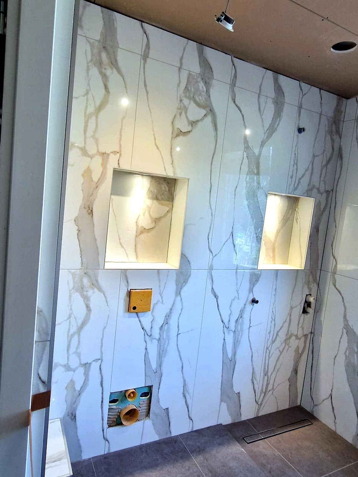 Douchewand in marmerlook met twee verlichte nissen en een vlakke vloergoot