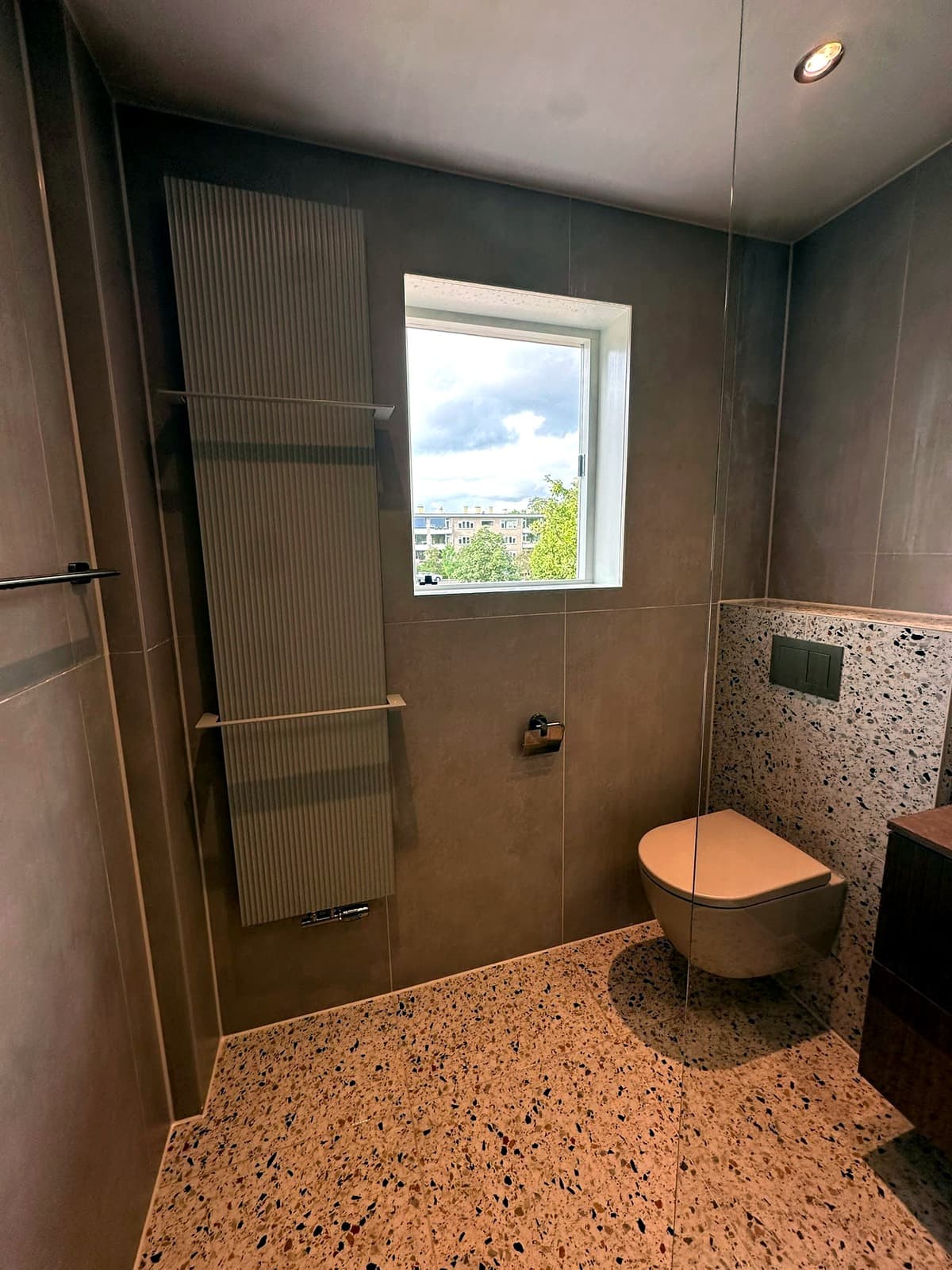 Toiletruimte met terrazzovloer, grote wandtegels en een hangend toilet